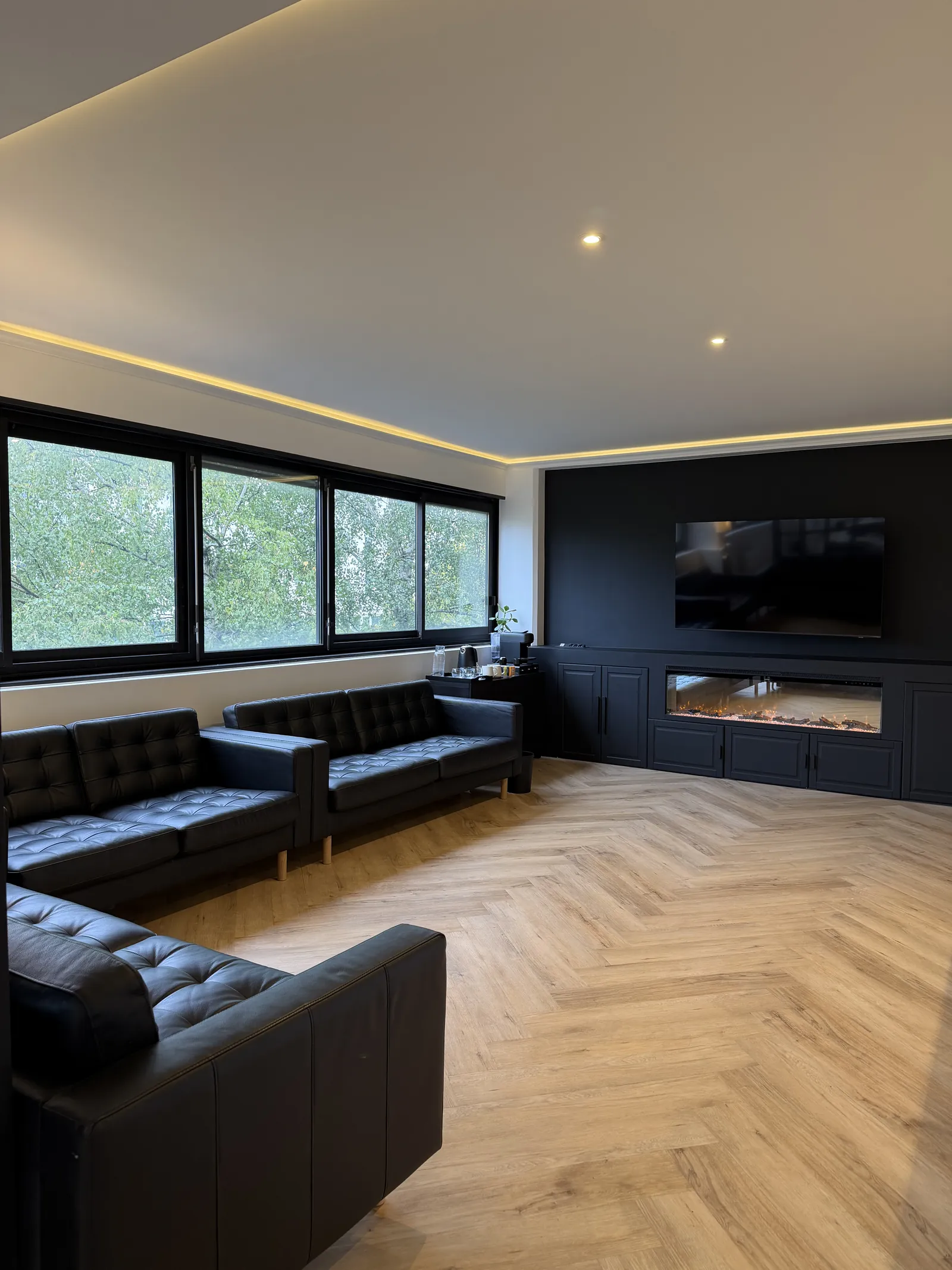 Le lounge de l'office : canapés en cuir noir, parquet à chevrons, cheminée et éclairage doré